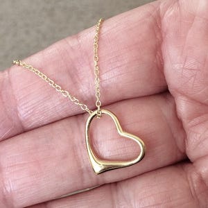May include: A gold-toned necklace featuring a delicate chain and an open, hollow heart-shaped pendant. The pendant is suspended from the chain, which consists of small, interconnected circular links. The metal has a smooth, polished finish.