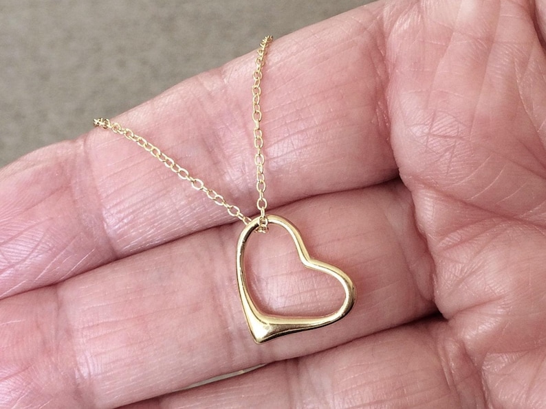 May include: A gold-toned necklace featuring a delicate chain and an open, hollow heart-shaped pendant. The pendant is suspended from the chain, which consists of small, interconnected circular links. The metal has a smooth, polished finish.