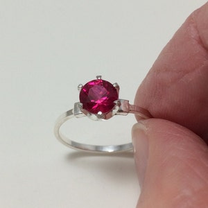 May include: A silver ring with a bright red gemstone set in a prong setting.