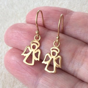 以下が含まれることがあります： ゴールドの天使のドロップイヤリングのペア。イヤリングは繊細な金属製で、翼のある天使のカットアウトデザインが施されています。