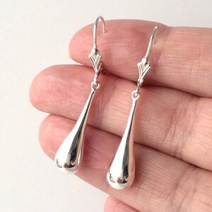 May include: A pair of silver teardrop dangle earrings. The earrings are made of smooth, polished metal and have a simple, elegant design.