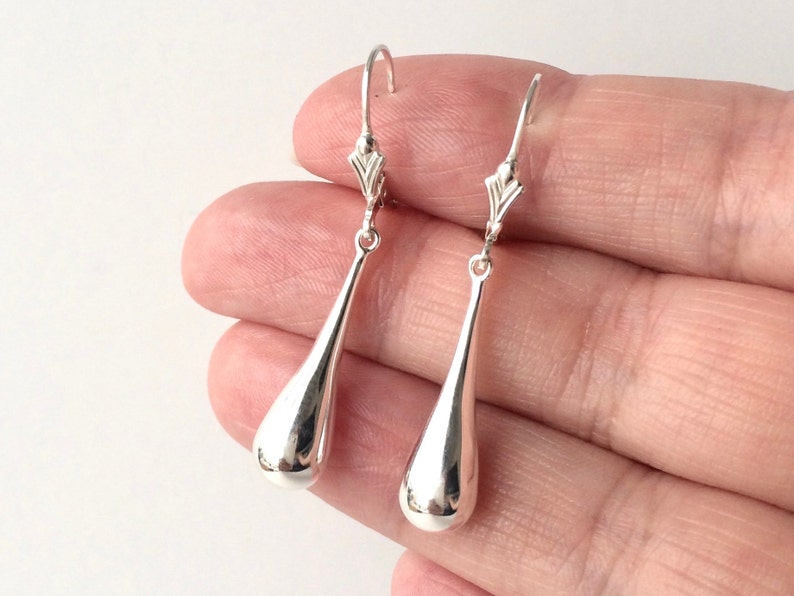 May include: A pair of silver teardrop dangle earrings. The earrings are made of smooth, polished metal and have a simple, elegant design.