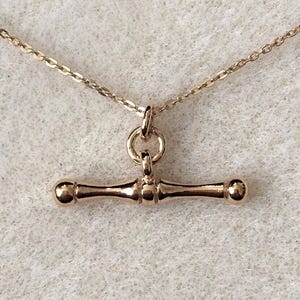 May include: A rose gold-coloured necklace featuring a T-bar toggle pendant suspended from a delicate cable chain. The pendant consists of a horizontal bar with rounded ends, connected to the chain by a small circular jump ring, creating a classic design.