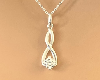 Puede incluir: Un collar de plata con un colgante que presenta un símbolo de infinito con una sola piedra transparente en el centro.