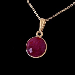 May include: A gold chain necklace with a pendant featuring a round, faceted ruby gemstone.