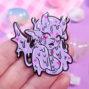 Może przedstawiać: Fioletowa szpilka emaliowana z postacią z kreskówki, która kapie, jest lepka, z różowymi sercami i różowo-białym tłem.