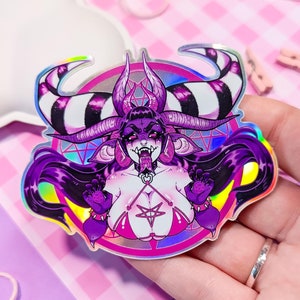 May include: A holographic sticker featuring a purple demon with horns, long black hair, and a pentagram symbol. The demon is wearing a pink and black bikini and a choker with a pentagram pendant. The sticker has a rainbow iridescent finish.