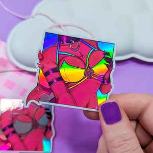 May include: A holographic sticker featuring a pink and red figure with rainbow accents wearing a yellow and rainbow bikini top and a black choker with a silver ring. The figure has horns and a tail.
