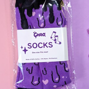 May include: Purple and black socks with a dripping design and hearts. The socks are packaged in a clear plastic bag with a white label that reads "CHAO SOCKS One size fits most Made of 82% Cotton, 15% Nylon, 3% Elastane".