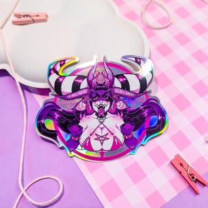 May include: A holographic sticker featuring a purple demon with horns and a pentagram. The demon is wearing a black and white striped collar and a red and black harness. The sticker is on a pink and white checkered background.