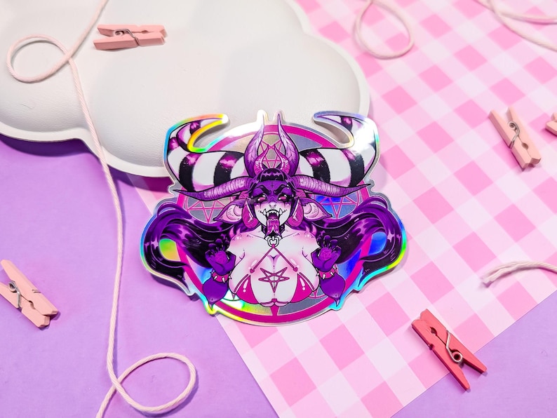 May include: A holographic sticker featuring a purple demon with horns and a pentagram. The demon is wearing a black and white striped collar and a red and black harness. The sticker is on a pink and white checkered background.