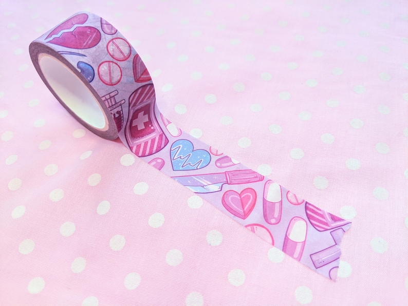 May include: A roll of pink washi tape with a pattern of hearts, pills, and medical symbols. The tape is on a pink background with white polka dots.