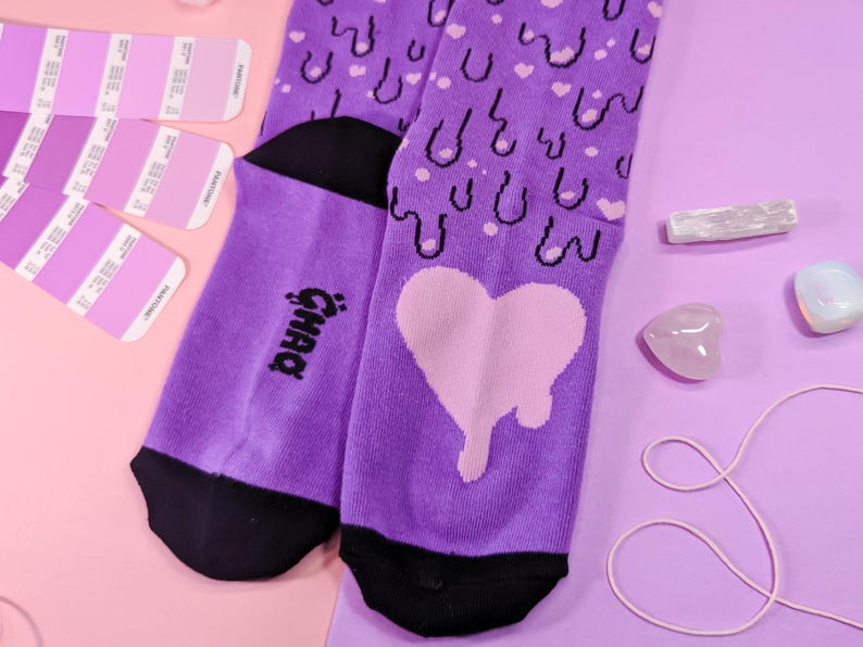May include: Purple socks with a dripping heart and a repeating pattern of hearts and drips. The socks have a black heel and toe. The text "Gnar" is printed on the side of the sock.