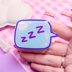 May include: A blue and purple speech bubble with the text "zzz" inside. The speech bubble is made of acrylic and has a glossy finish.