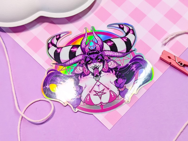May include: A holographic sticker featuring a purple demon with black and white horns, a pentagram, and a rainbow. The demon is wearing a pink bikini top with a pentagram.