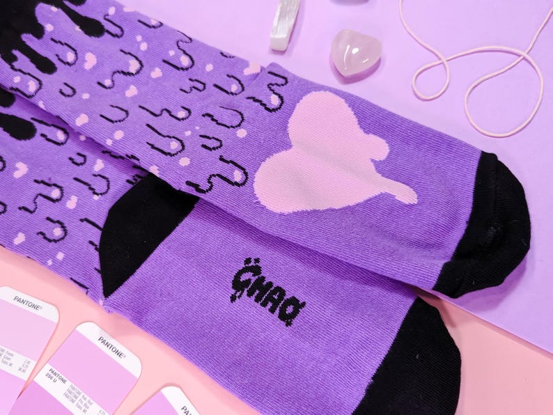 May include: Purple and black socks with a pink heart and dripping black paint design. The socks have the word "GHAD" written on them.