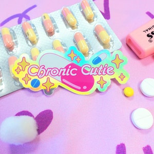 May include: A pink and yellow pill sticker with the text "Chronic Cutie" in a rainbow font. The sticker is surrounded by glitter and stars. There are also several pink and yellow pills in a blister pack, white and yellow pills, and two pink highlighters.