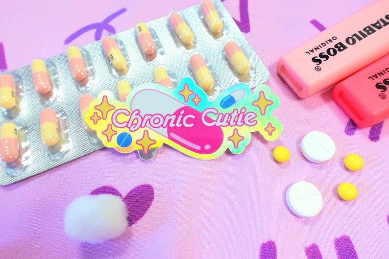 May include: A pink and yellow pill sticker with the text "Chronic Cutie" in a rainbow font. The sticker is surrounded by glitter and stars. There are also several pink and yellow pills in a blister pack, white and yellow pills, and two pink highlighters.