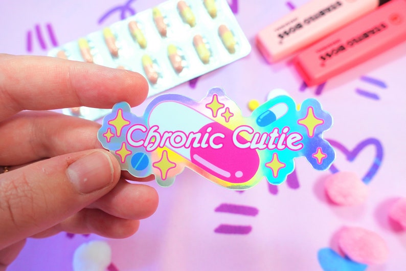 May include: A holographic sticker with a pink pill design and the text "Chronic Cutie". The sticker has a rainbow iridescent finish and features glitter stars.