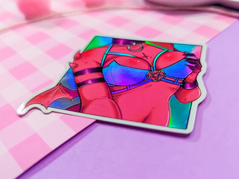 Może przedstawiać: Holograficzna naklejka przedstawiająca czerwonosk&oacute;rą postać z rogami i skrzydłami, ubraną w niebieski i fioletowy, tęczowy top bikini z pentagramem. Postać ma czerwoną i czarną obrożę z srebrnym pierścieniem.