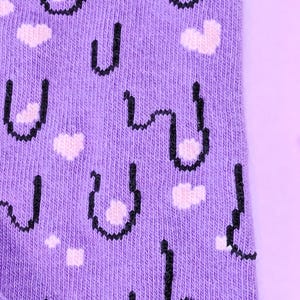 May include: Purple socks with a pixelated design of a face with hearts. The socks have a black outline and pink hearts.