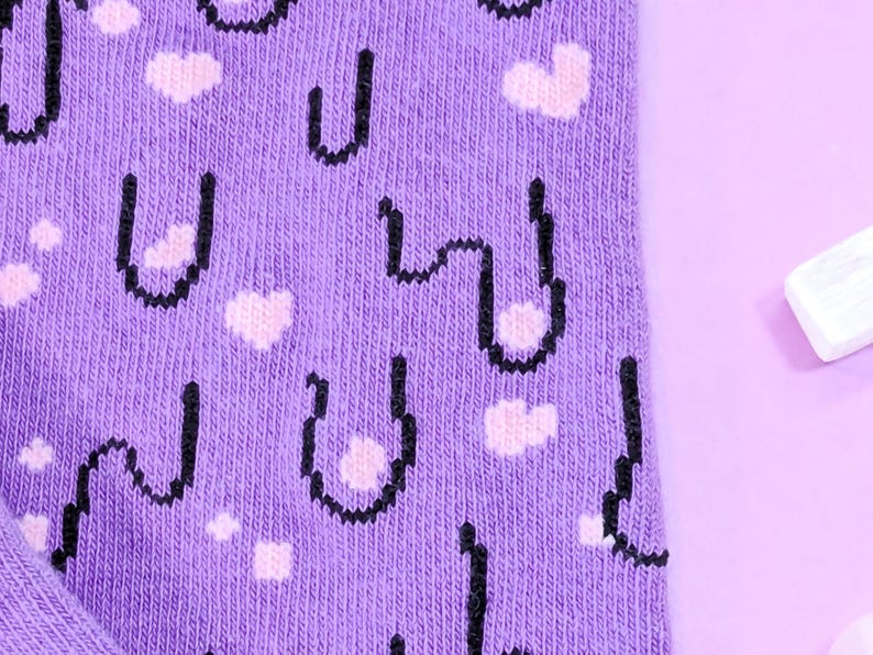 May include: Purple socks with a pixelated design of a face with hearts. The socks have a black outline and pink hearts.