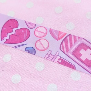 May include: A purple and pink patterned washi tape with a broken heart, pills, bandages, and a bottle with a cross on it.