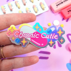May include: A holographic sticker with a pink and white pill design. The sticker says "Chronic Cutie" in a rainbow font.