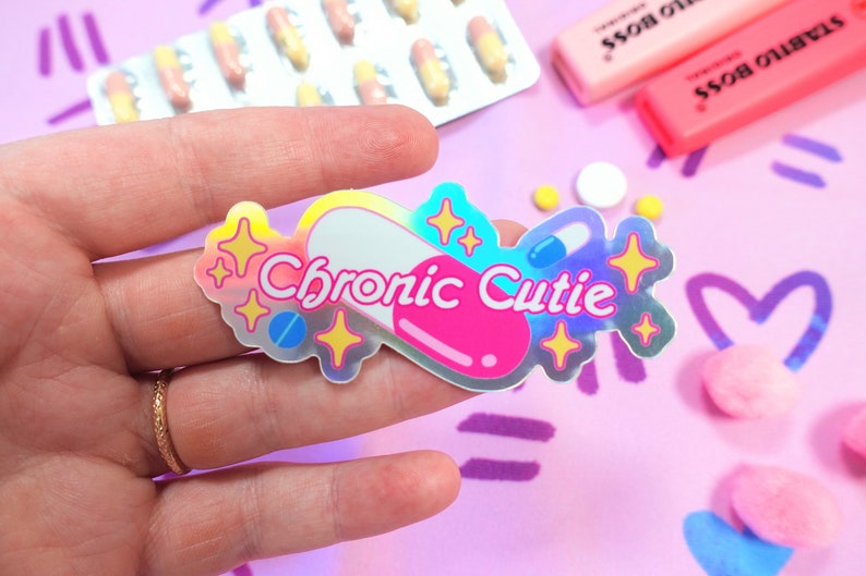 May include: A holographic sticker with a pink and white pill design. The sticker says "Chronic Cutie" in a rainbow font.