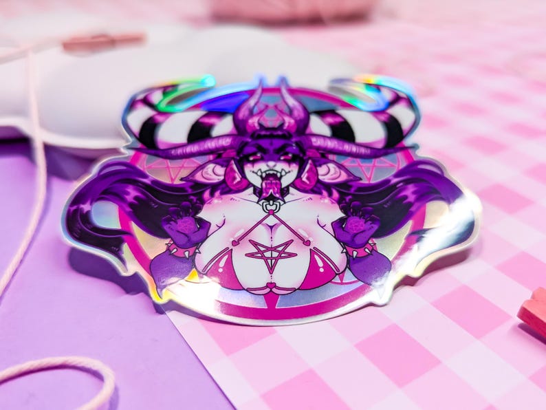 May include: A holographic sticker featuring a purple-haired demon with horns, wearing a pink bikini and a pentagram necklace. The demon is surrounded by a pink and white circle with a pentagram design.