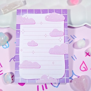 May include: A lined notepad with a purple grid border and cloud and star illustrations. The notepad has a white interior with horizontal lines for writing. The background is a light purple with decorative elements.