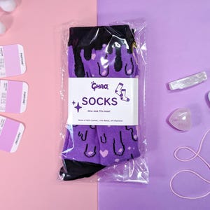 May include: Purple and black socks with a dripping ice cream cone design. The socks are packaged in a clear plastic bag with a white label that reads "Ghaa Socks" and "One size fits most".