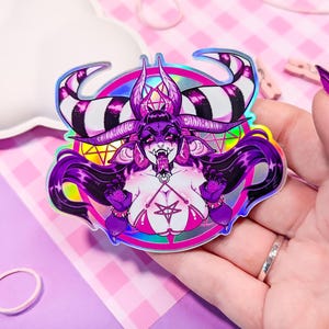 May include: A holographic sticker featuring a purple and black demon with horns, a pentagram, and a pink and white bikini. The demon is surrounded by a rainbow halo.