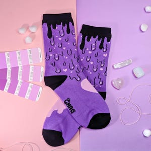 May include: A pair of purple socks with a black dripping design and pink hearts. The socks have the word "CHAD" written on one sock.