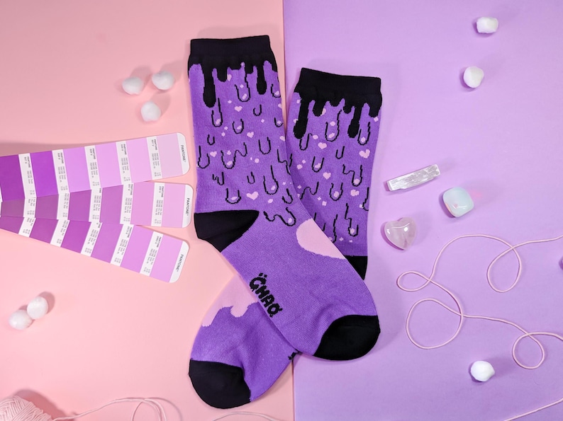 May include: A pair of purple socks with a black dripping design and pink hearts. The socks have the word "CHAD" written on one sock.