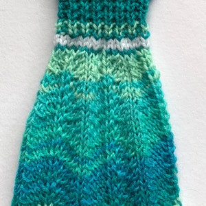 Könnte beinhalten: Ein gestricktes Kleid mit einem weißen Häkel-Oberteil und einem grün-blau-weiß gestreiften Muster.