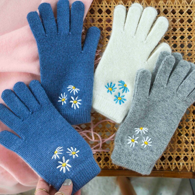 K&ouml;nnte beinhalten: Vier Paar Strickhandschuhe mit gestickten wei&szlig;en G&auml;nsebl&uuml;mchen. Die Handschuhe sind in Blau, Wei&szlig; und Grau.
