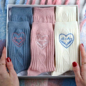 Könnte beinhalten: Eine Geschenkbox mit drei Paar Socken. Die Socken sind in Blau, Rosa und Weiß. Jedes Paar hat ein Herz mit den Initialen "S+A" bestickt.