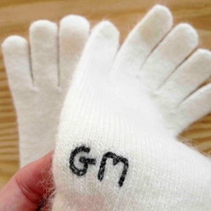 Puede incluir: Guantes de punto blancos con un logotipo "GM" negro en la mu&ntilde;eca.