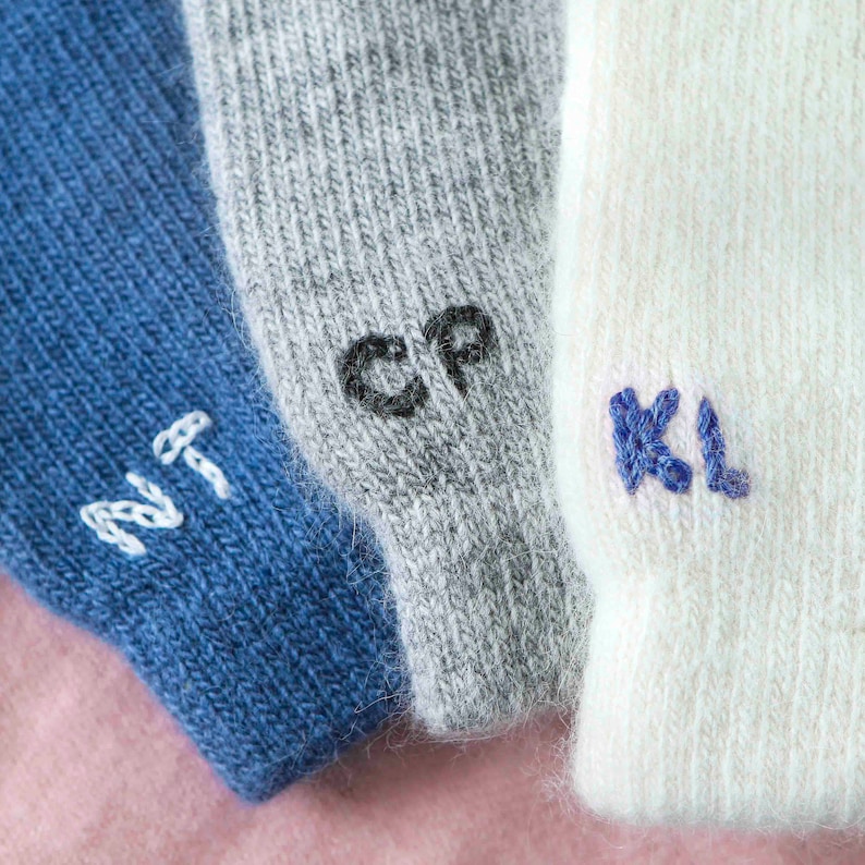 K&ouml;nnte beinhalten: Drei Paar Socken mit gestickten Initialen. Die Socken sind blau, grau und wei&szlig;.
