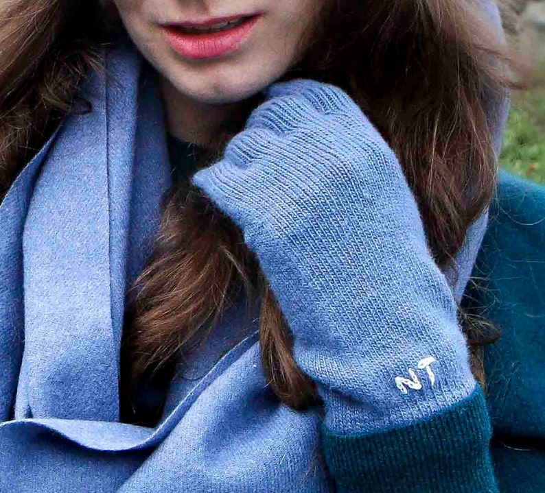 Puede incluir: Un par de guantes de punto azul con un monograma bordado en blanco "NT" en el pu&ntilde;o.