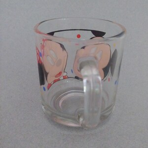 May include: A clear glass mug with a handle. The mug has a cartoon image of Mickey Mouse and Minnie Mouse on it. The image is surrounded by colorful polka dots.