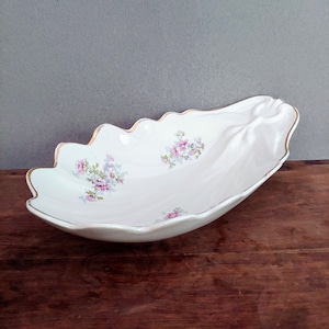 May include: A white ceramic serving dish with a scalloped edge and a gold trim. The dish is decorated with a floral pattern in shades of pink and blue.