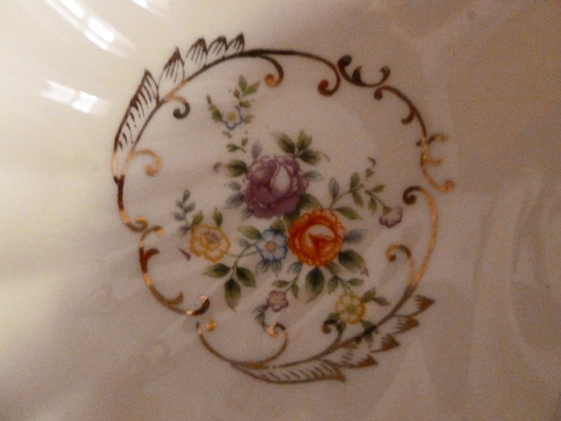 May include: A white ceramic bowl with a gold floral design. The design features pink, yellow, and white flowers with green leaves.