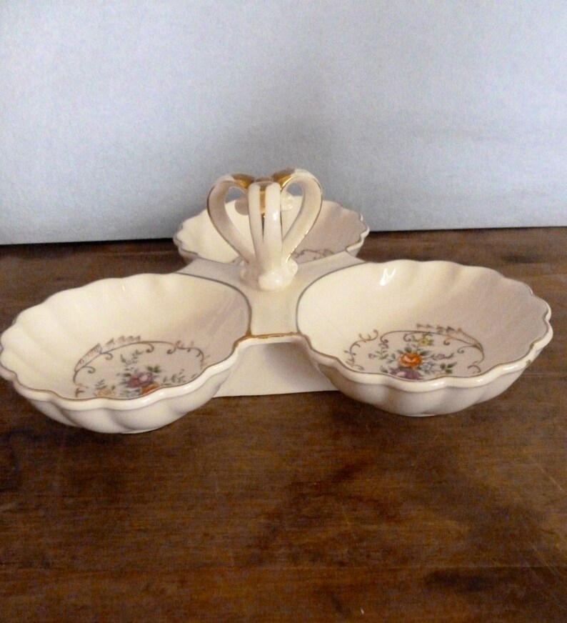 May include: A white ceramic three-section serving dish with a gold handle and floral design.