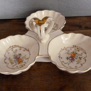 May include: A white ceramic three-section serving dish with a gold handle and floral designs. Each section has a scalloped edge and a gold rim.