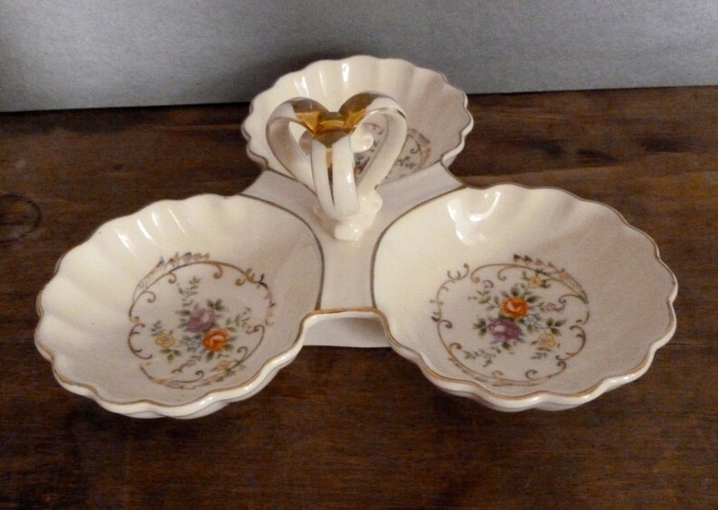 May include: A white ceramic three-section serving dish with a gold handle and floral designs. Each section has a scalloped edge and a gold rim.