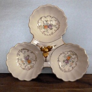May include: A white ceramic three-section serving dish with a gold trim and floral design. The dish has a central handle with a gold ball finial.