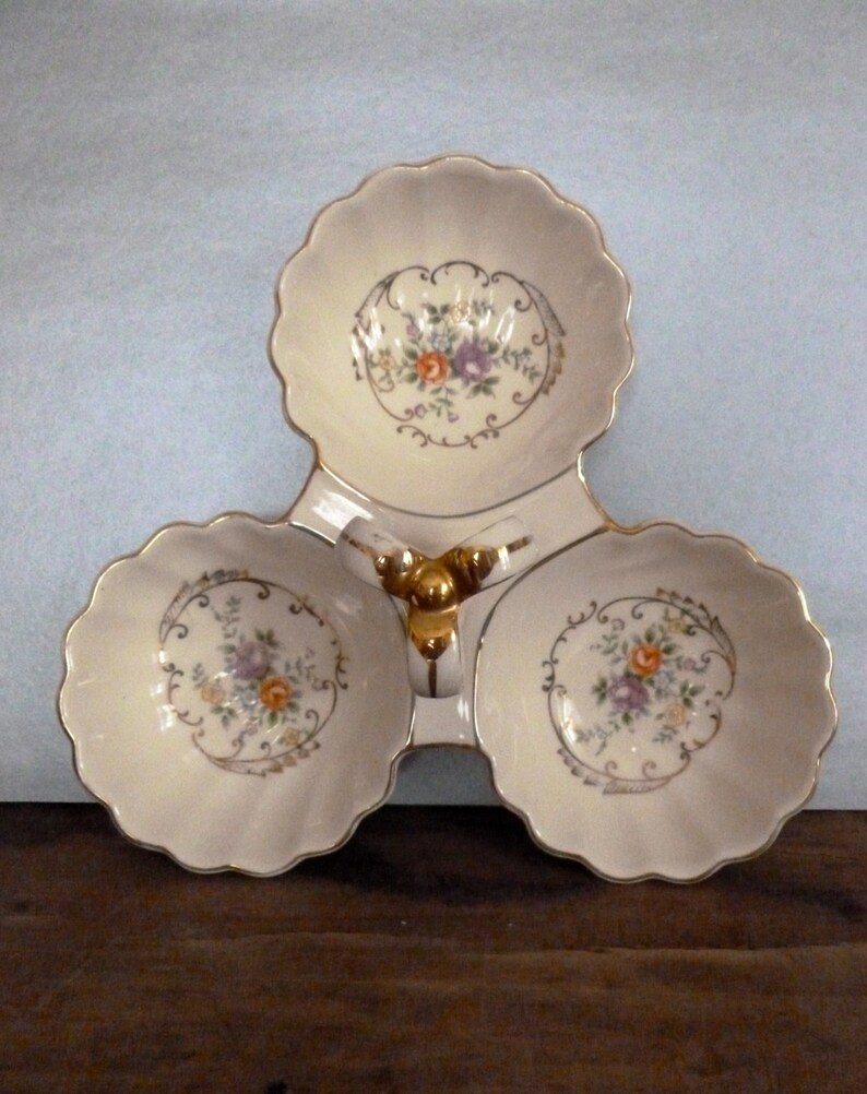 May include: A white ceramic three-section serving dish with a gold trim and floral design. The dish has a central handle with a gold ball finial.