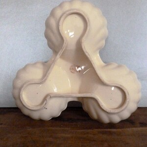 May include: A white ceramic serving dish with three sections, each shaped like a scallop shell. The dish is designed to hold three different types of food.